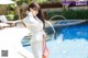 A woman in a white suit standing next to a swimming pool.