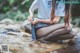 A woman sitting on a rock in a stream.