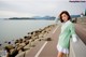 A woman in a green sweater leaning against a wall by the water.